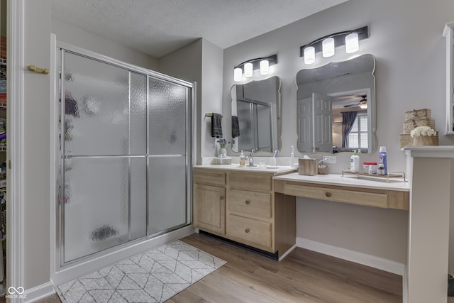 full bath with a stall shower, wood finished floors, vanity, ceiling fan, and a textured ceiling