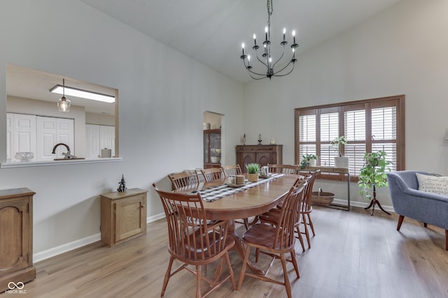 dining space featuring high vaulted ceiling, light wood-type flooring, a chandelier, and baseboards