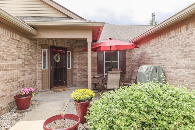 property entrance featuring a shingled roof, brick siding, and a patio area