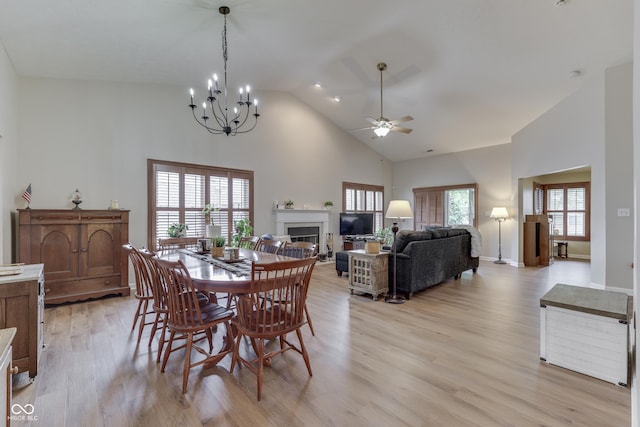 dining area with high vaulted ceiling, a ceiling fan, light wood-type flooring, a glass covered fireplace, and a chandelier