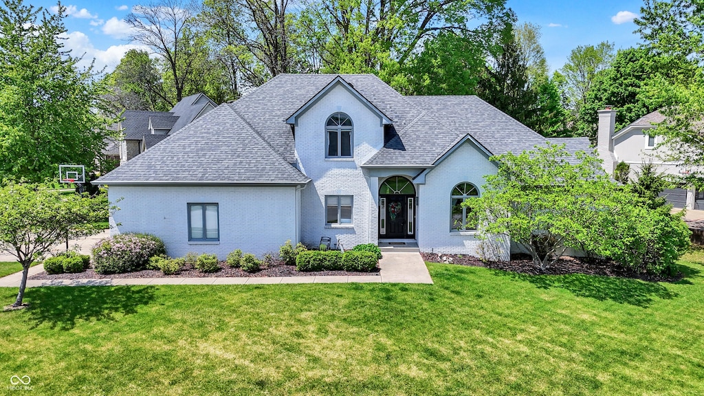view of front of property featuring a shingled roof, a front yard, and brick siding