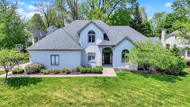 view of front of property featuring a shingled roof, a front yard, and brick siding