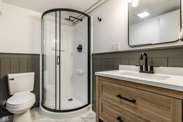 bathroom featuring a shower stall, a wainscoted wall, toilet, vanity, and a decorative wall