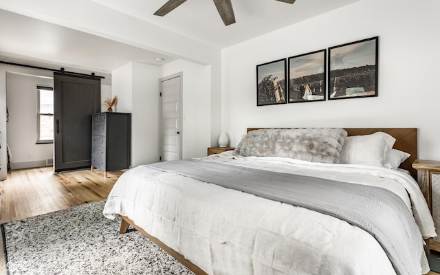 bedroom featuring wood finished floors, a barn door, and ceiling fan