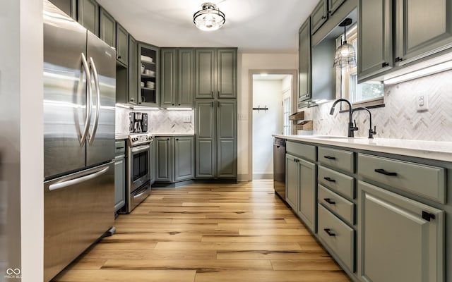 kitchen with appliances with stainless steel finishes, tasteful backsplash, light countertops, light wood-style flooring, and a sink