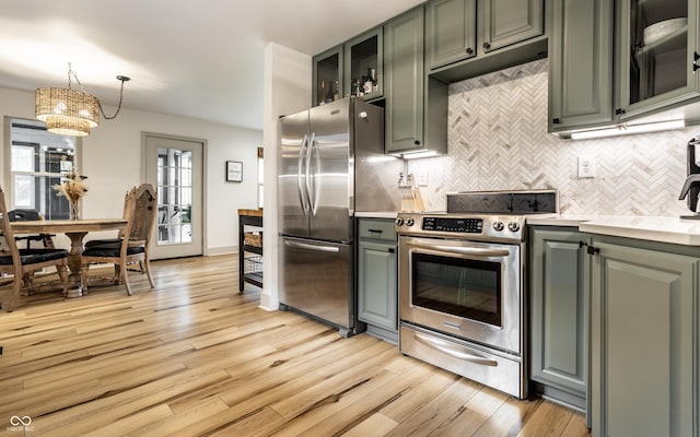 kitchen with stainless steel appliances, backsplash, light countertops, light wood-style flooring, and hanging light fixtures