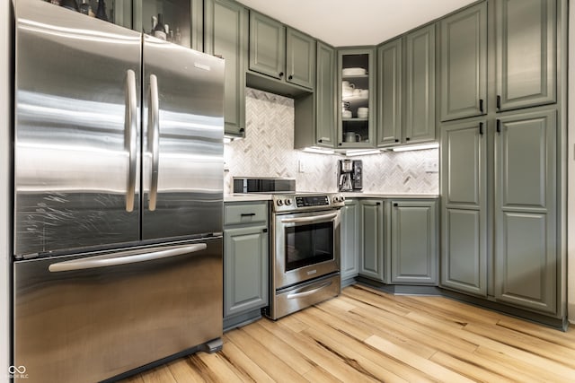 kitchen with stainless steel appliances, light wood-style floors, tasteful backsplash, glass insert cabinets, and light countertops