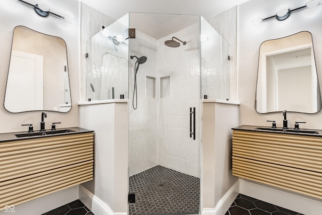 bathroom featuring tile patterned flooring, a shower stall, baseboards, and two vanities