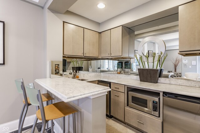 kitchen featuring stainless steel appliances, a kitchen bar, a peninsula, light stone countertops, and recessed lighting