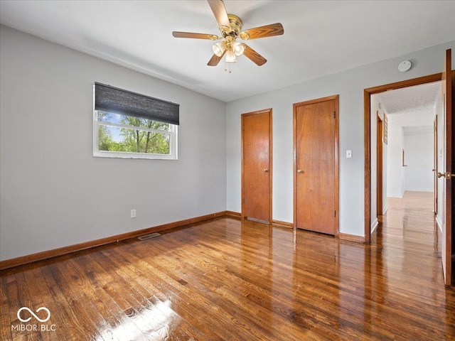 unfurnished bedroom featuring two closets, wood finished floors, baseboards, and ceiling fan