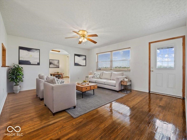 living area with arched walkways, hardwood / wood-style flooring, a ceiling fan, a textured ceiling, and plenty of natural light