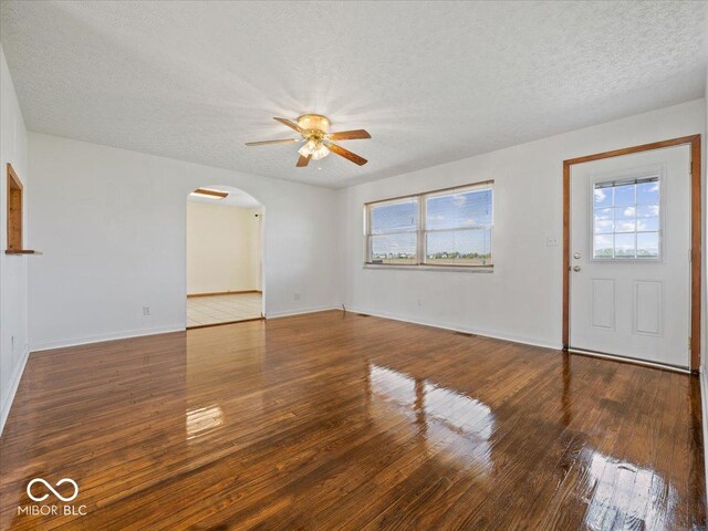 unfurnished living room featuring a ceiling fan, a textured ceiling, arched walkways, healthy amount of natural light, and hardwood / wood-style flooring