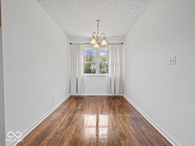 unfurnished dining area with a chandelier, dark wood-type flooring, a textured ceiling, and baseboards