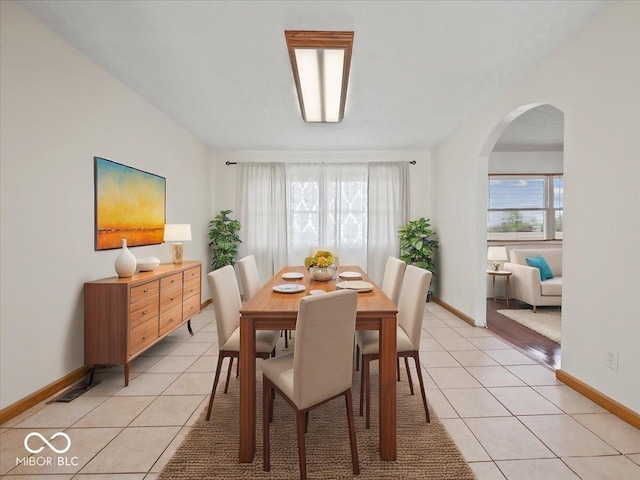 dining room featuring arched walkways, light tile patterned flooring, and baseboards