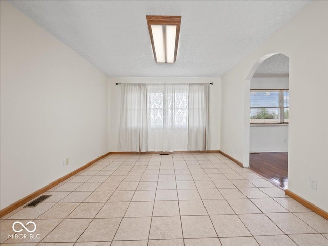 unfurnished room featuring arched walkways, baseboards, a textured ceiling, and light tile patterned floors