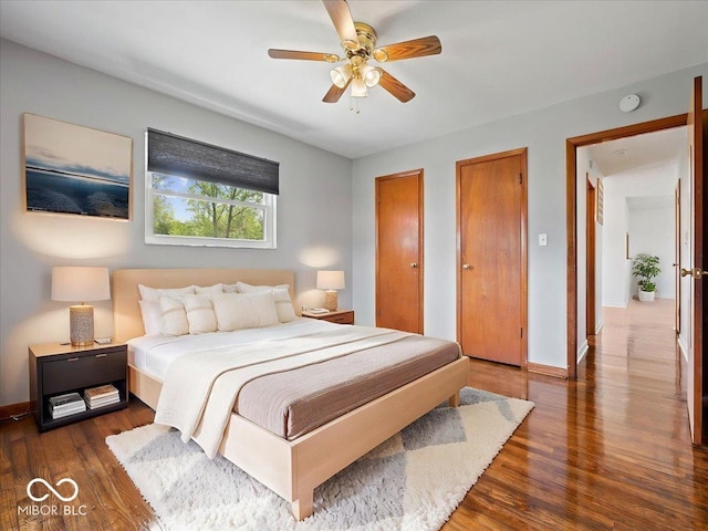 bedroom with two closets, wood finished floors, baseboards, and ceiling fan