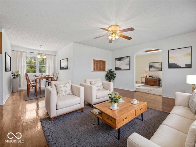 living area with arched walkways, wood finished floors, a textured ceiling, a ceiling fan, and baseboards
