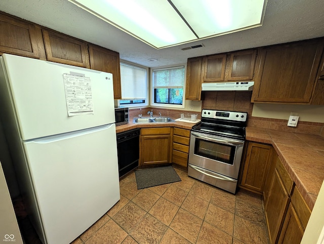 kitchen with appliances with stainless steel finishes, under cabinet range hood, a sink, tile counters, and light tile patterned flooring