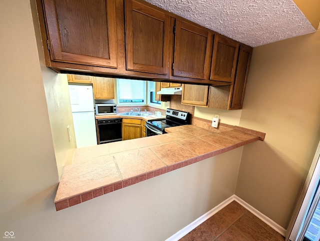 kitchen featuring appliances with stainless steel finishes, under cabinet range hood, light countertops, baseboards, and a sink