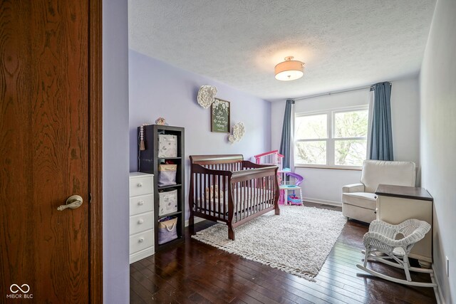 bedroom with dark wood-style floors, a textured ceiling, a nursery area, and baseboards