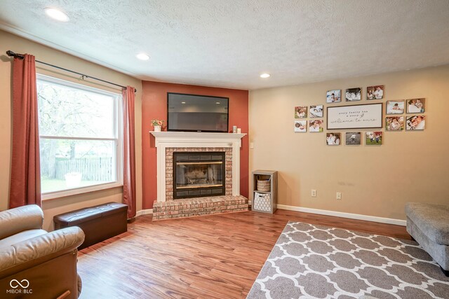 living room featuring wood finished floors, a textured ceiling, a brick fireplace, recessed lighting, and baseboards