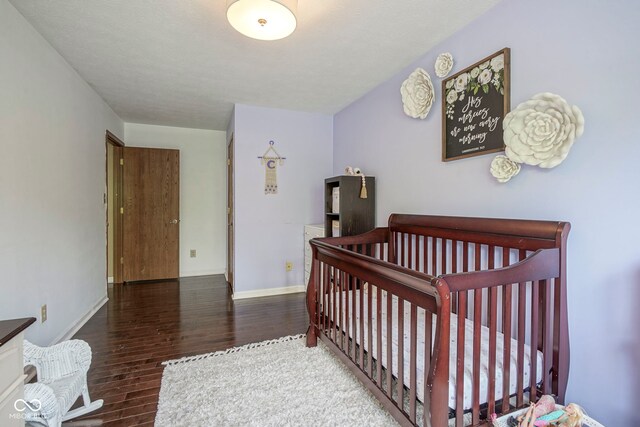bedroom with wood finished floors, baseboards, and a crib