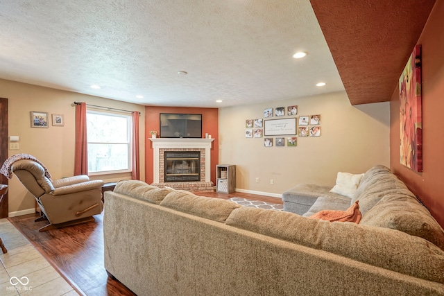 living room featuring a textured ceiling, a brick fireplace, recessed lighting, baseboards, and light wood finished floors
