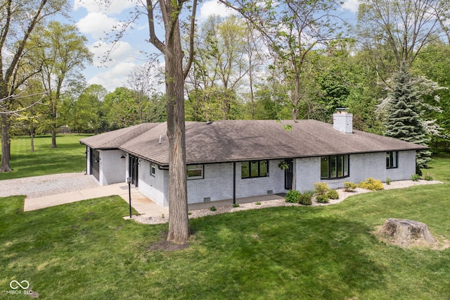 back of house featuring gravel driveway, a chimney, a lawn, and brick siding