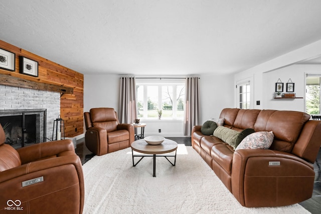 living room featuring healthy amount of natural light, wood walls, an accent wall, a brick fireplace, and wood finished floors