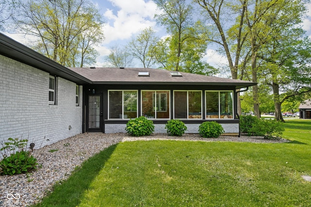 rear view of property with a sunroom, a lawn, and brick siding