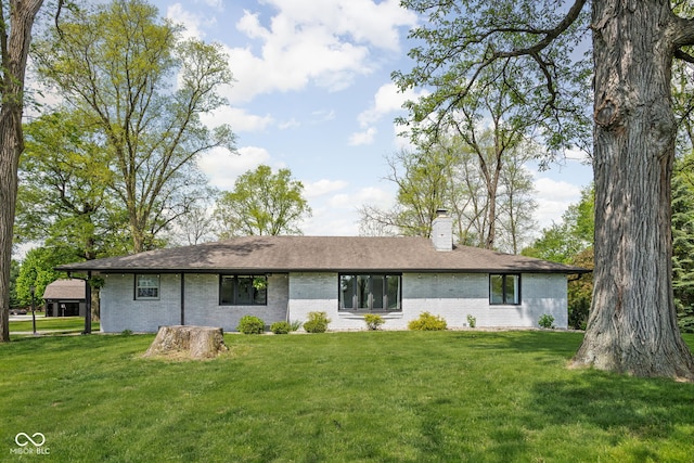 back of house with a chimney, brick siding, and a yard