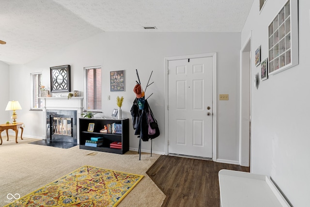 foyer entrance featuring a textured ceiling, a fireplace with flush hearth, lofted ceiling, baseboards, and wood finished floors