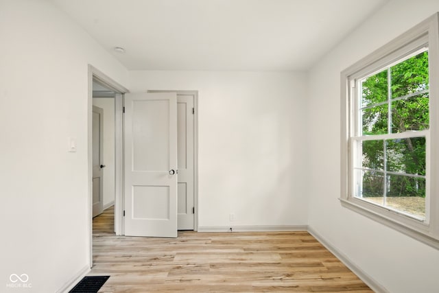 empty room featuring plenty of natural light, light wood-style flooring, baseboards, and a smoke detector
