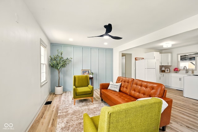 living room featuring a ceiling fan, light wood-style floors, a decorative wall, and baseboards