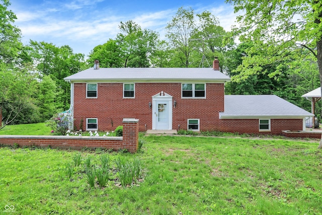 bi-level home featuring a chimney, a front lawn, brick siding, and view of wooded area