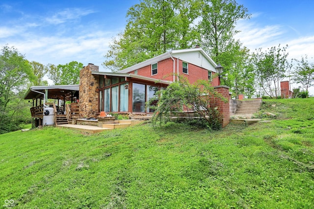 back of property with a chimney, a lawn, and a sunroom