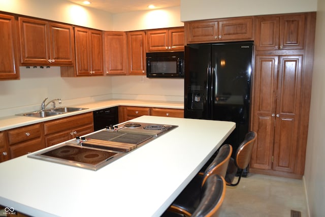 kitchen with black appliances, a sink, brown cabinetry, light countertops, and a breakfast bar