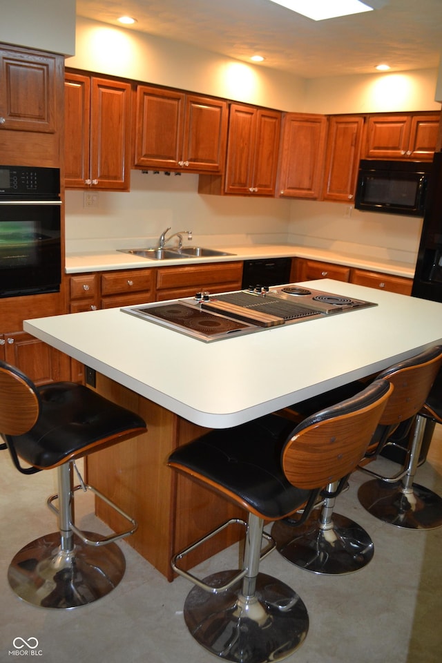 kitchen with black appliances, a kitchen breakfast bar, a sink, brown cabinetry, and light countertops