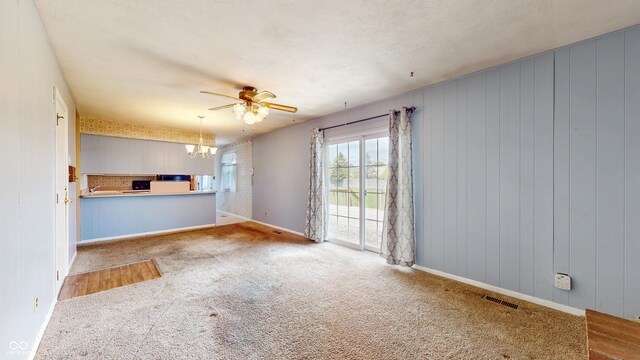 unfurnished living room featuring a chandelier, carpet floors, a ceiling fan, and baseboards