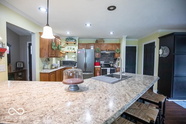 kitchen with appliances with stainless steel finishes, a sink, brown cabinetry, a kitchen bar, and ornamental molding