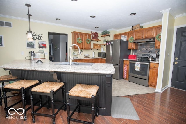 kitchen with appliances with stainless steel finishes, under cabinet range hood, a sink, a peninsula, and brown cabinets