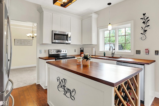 kitchen with wood counters, appliances with stainless steel finishes, a sink, a chandelier, and dark wood-style floors