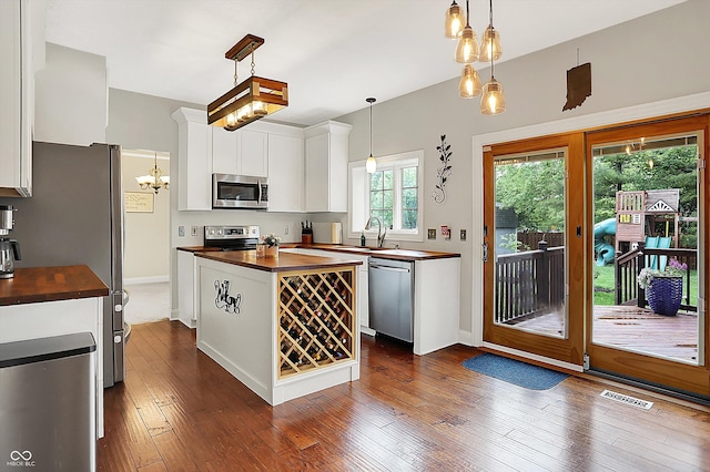 kitchen with wooden counters, appliances with stainless steel finishes, a sink, white cabinetry, and baseboards