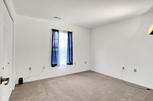 carpeted spare room featuring a textured ceiling and baseboards