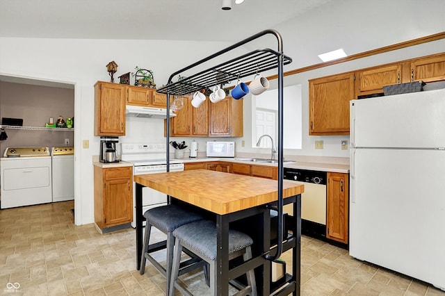 kitchen with white appliances, independent washer and dryer, a sink, under cabinet range hood, and stone finish floors