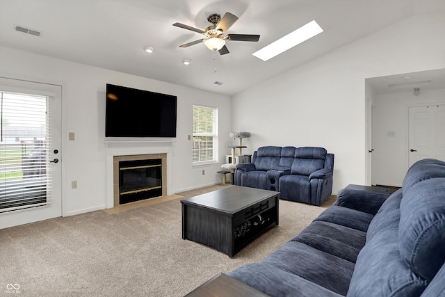 living room with a ceiling fan, vaulted ceiling, light carpet, a tile fireplace, and a skylight
