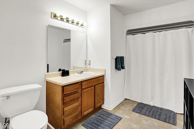 bathroom featuring toilet, vanity, stone finish floors, baseboards, and curtained shower