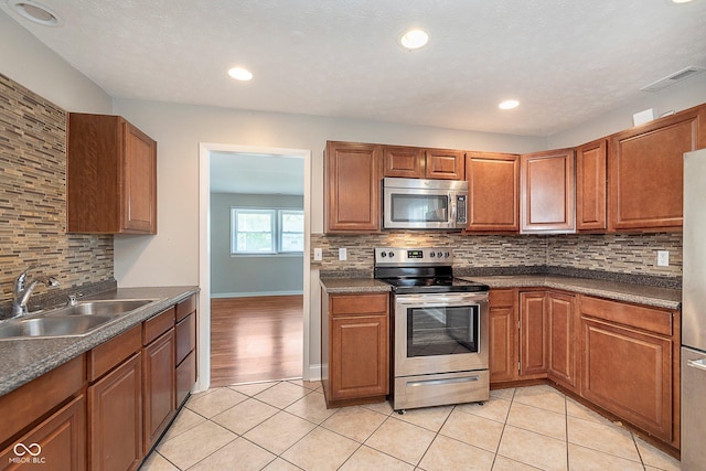 kitchen featuring appliances with stainless steel finishes, a sink, decorative backsplash, dark countertops, and light tile patterned flooring