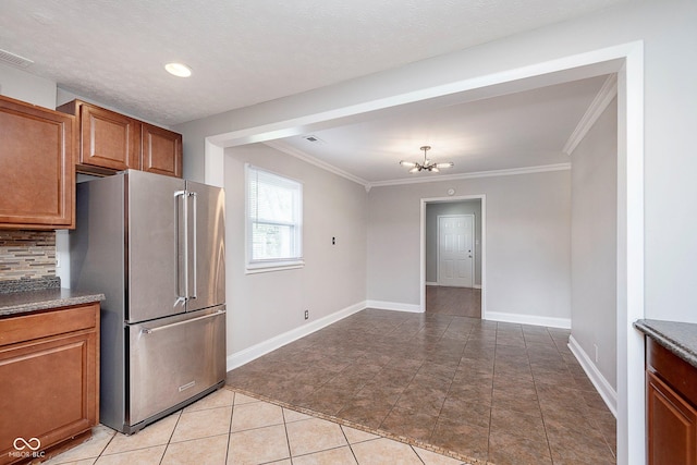 kitchen featuring freestanding refrigerator, brown cabinetry, crown molding, backsplash, and baseboards