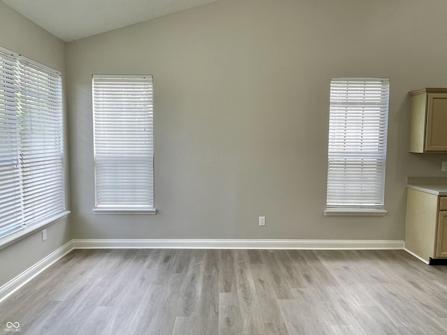 spare room featuring light wood-style floors, vaulted ceiling, and baseboards